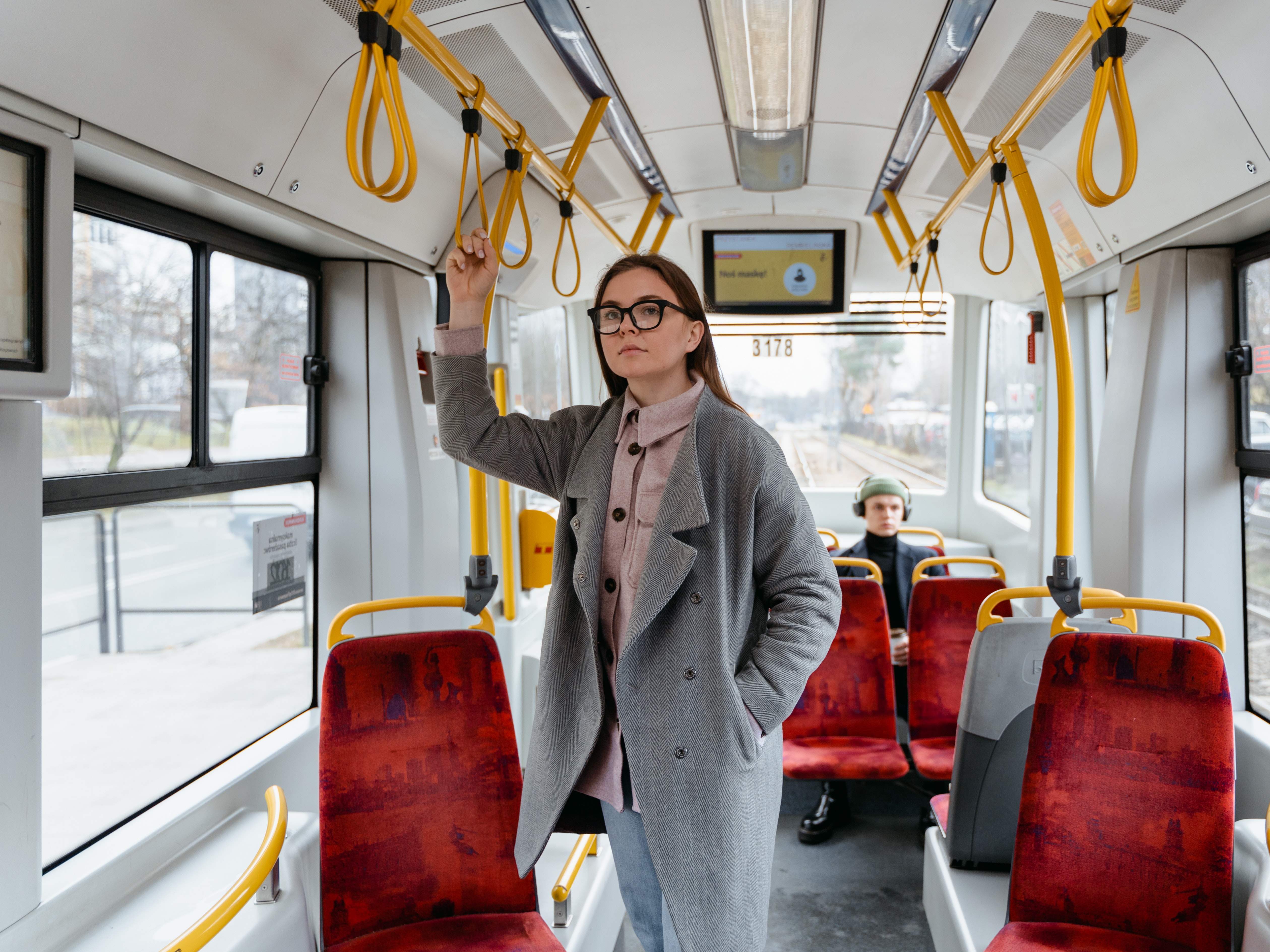 Femme de face dans un transport en commun type bus (fauteuils rouges et maintien jaune), ambiance blanche